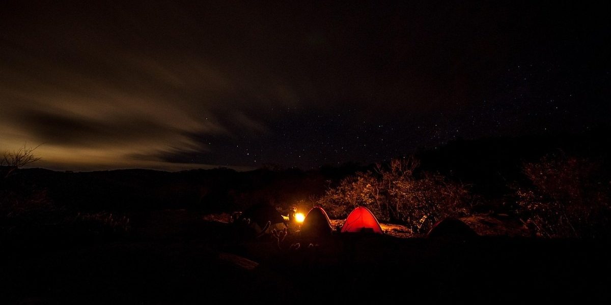 Campement de nuit en montagne avec tente rouge éclairée sous les étoiles