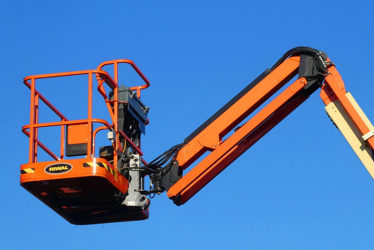 Plateforme orange élévatrice sur bras articulé contre ciel bleu
