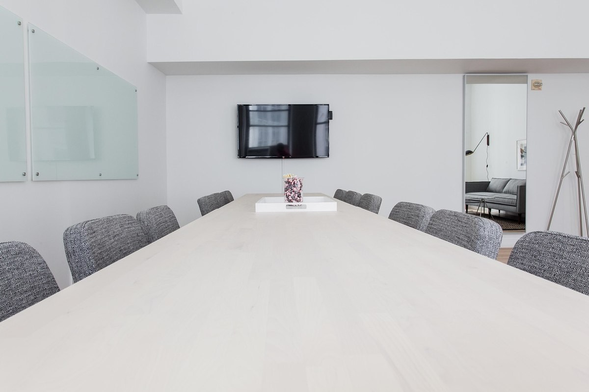 Salle de réunion professionnelle avec table ovale blanche, chaises grises et écran mural