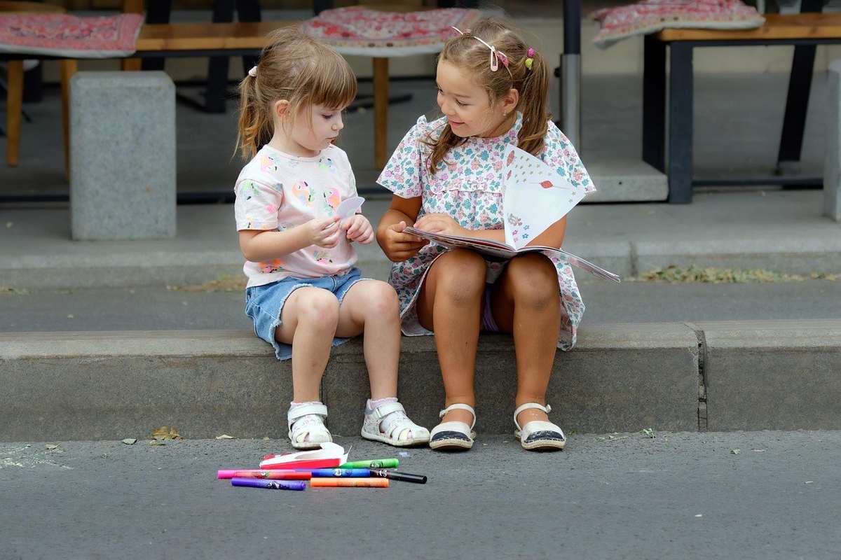 Filles lisant un livre sur le trottoir avec des feutres à proximité Filles lisant un livre sur le trottoir avec des feutres à proximité