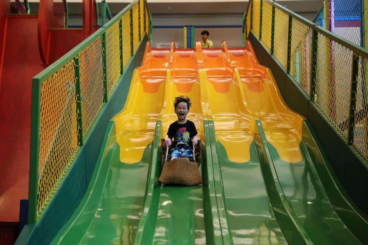 Enfant descendant un toboggan vert dans un parc de jeux intérieur Enfant descendant un toboggan vert dans un parc de jeux intérieur